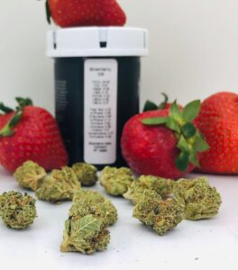 strawberry og strain buds with real strawberries and hms container showing terpene and potency label
